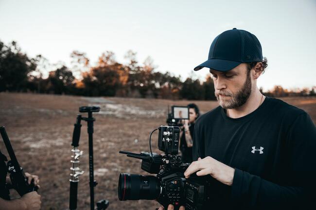 A person standing in a muddy field holding a DSLR camera rig.