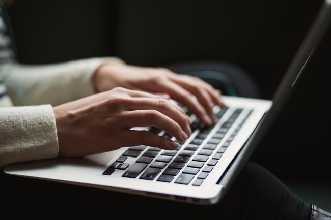 A closeup of a person's hands typing on a laptop keyboard.