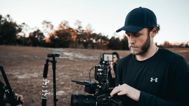 A person standing in a muddy field holding a DSLR camera rig.