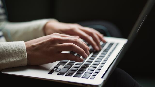A closeup of a person's hands typing on a laptop keyboard.